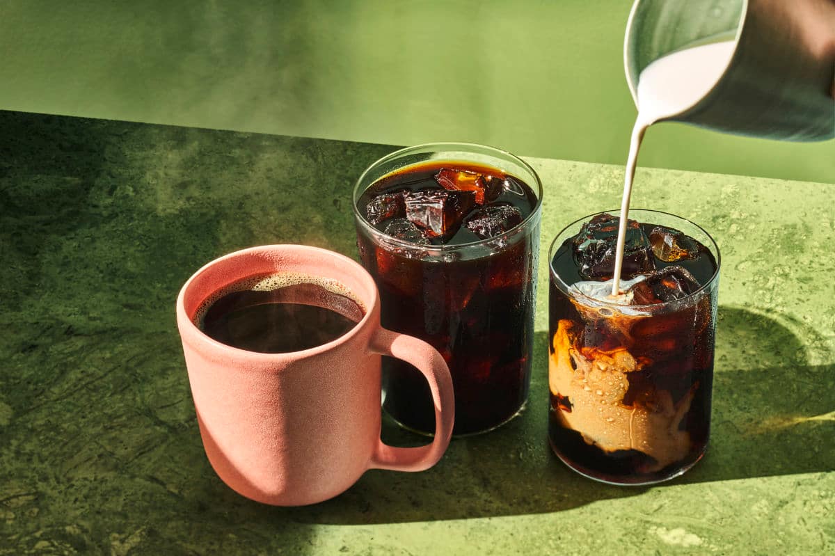 iced coffee pour in two glasses next to warm coffee mug
